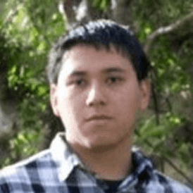 Person in checkered shirt outdoors, trees in background.